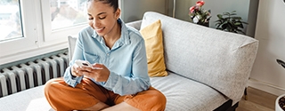 Woman on her mobile phone while sitting cross-legged on a couch.