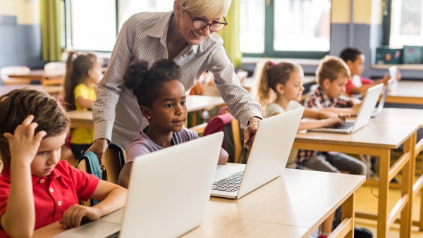 Teacher assisting elementary school kids working on laptops