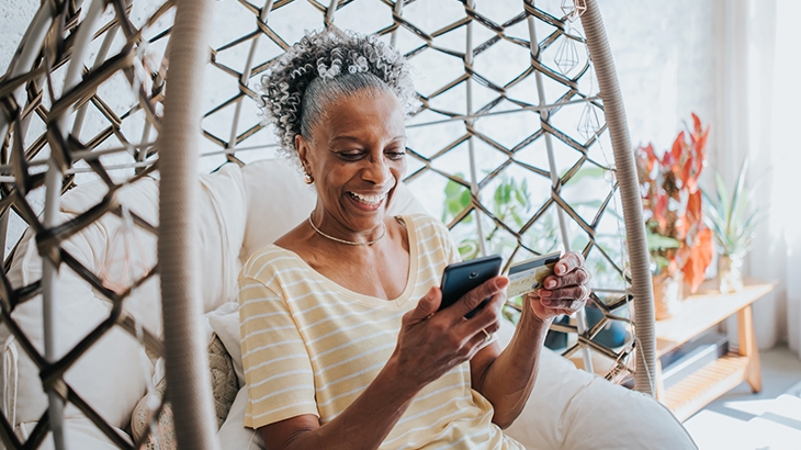 Woman using credit card holding her cell phone in living room