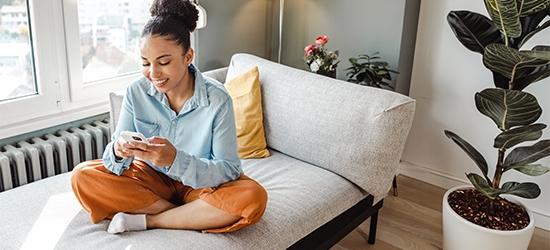 Woman on her mobile phone while sitting cross-legged on a couch.