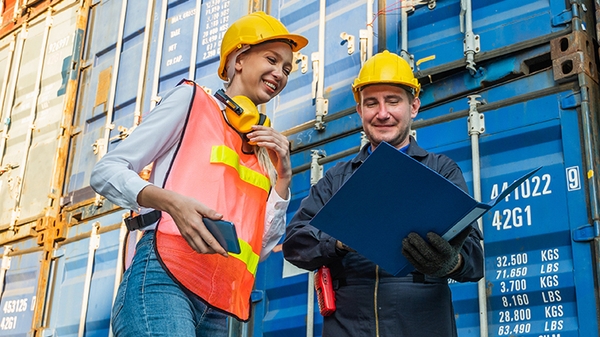 Two people in hardhats talking by shipping containers