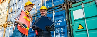 Two people in hardhats talking by shipping containers.