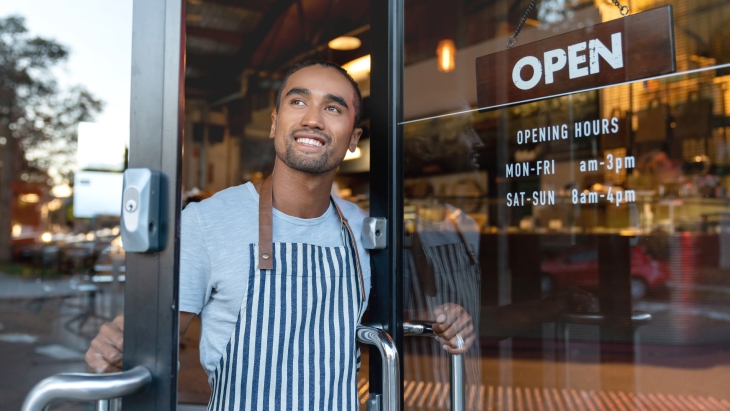 Happy shop owner opening doors at his cafe.