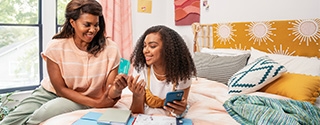 Mother and daughter smiling while looking at the green light app and credit card.