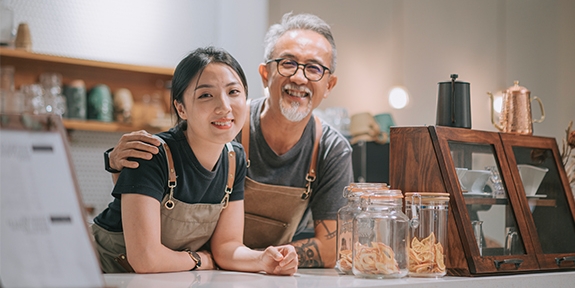 Padre e hija manejando en su cafetería, sonriendo en el mostrador.