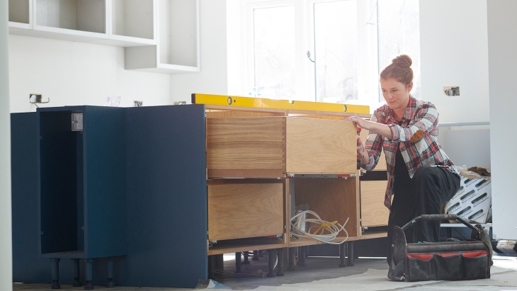 A woman installing kitchen cabinets.