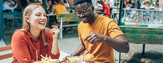 Amigos divirtiéndose comiendo hamburguesas y papas fritas en un restaurante al aire libre.