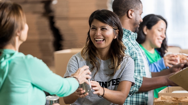 Volunteer smiling handing canned food to another person.