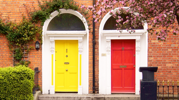 Yellow and red two doors with pink blooms and green ivies on the brick wall