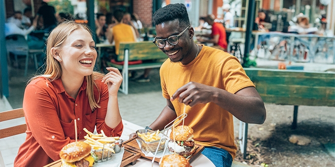 Amigos divirtiéndose comiendo hamburguesas y papas fritas en un restaurante al aire libre.