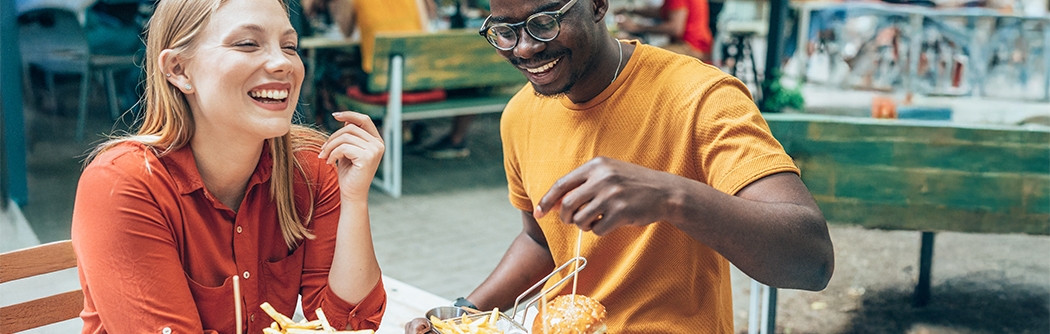 Amigos divirtiéndose comiendo hamburguesas y papas fritas en un restaurante al aire libre.