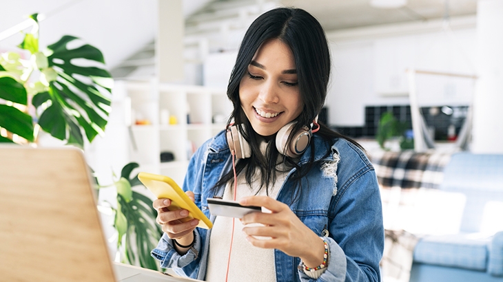 Woman doing online shopping at home with credit card and smartphone.