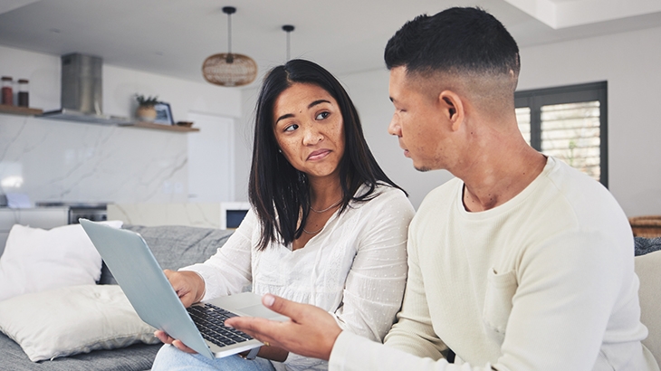 Couple looking sad at each other with laptop.