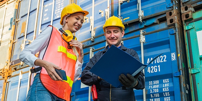 Two people in hardhats talking by shipping containers.