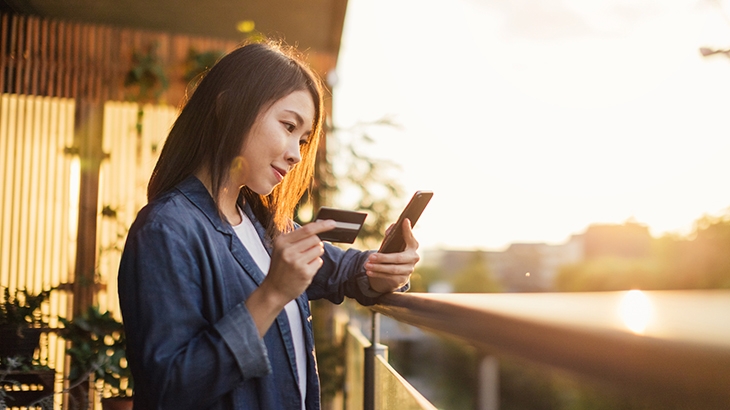 Woman holding credit card while shopping on phone outside.