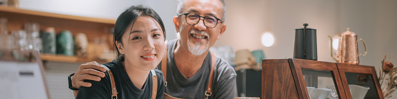 Padre e hija manejando en su cafetería, sonriendo en el mostrador.