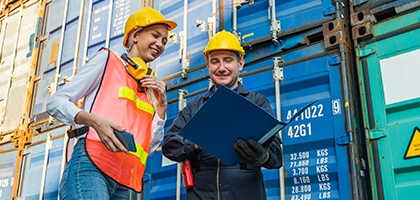 Two people in hardhats talking by shipping containers.