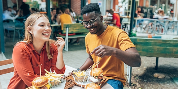 Amigos divirtiéndose comiendo hamburguesas y papas fritas en un restaurante al aire libre.