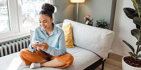 Woman on her mobile phone while sitting cross-legged on a couch.