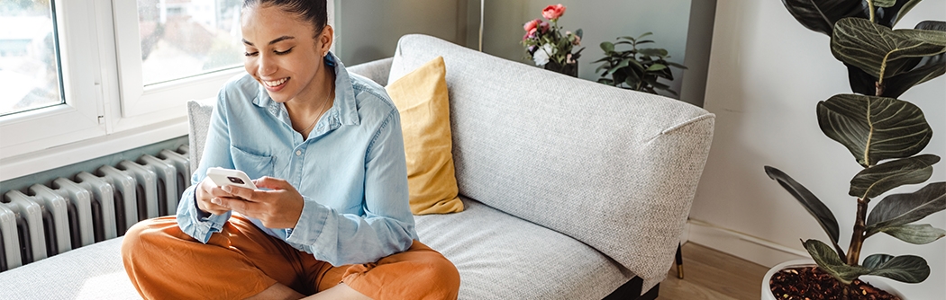 Woman on her mobile phone while sitting cross-legged on a couch.