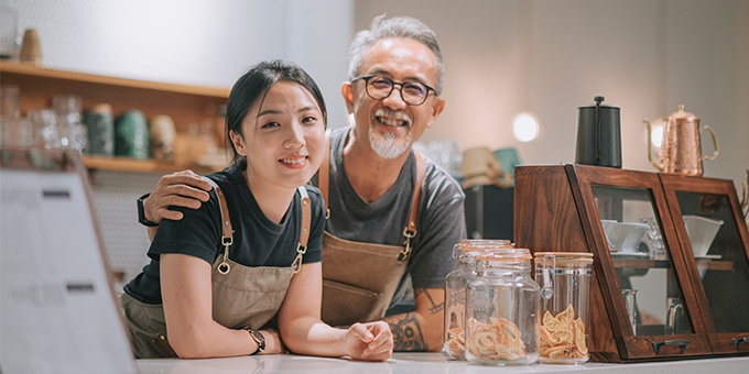 Padre e hija manejando en su cafetería, sonriendo en el mostrador.