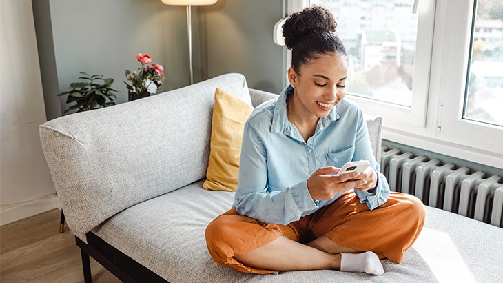 Woman on her mobile phone while sitting cross-legged on a couch.