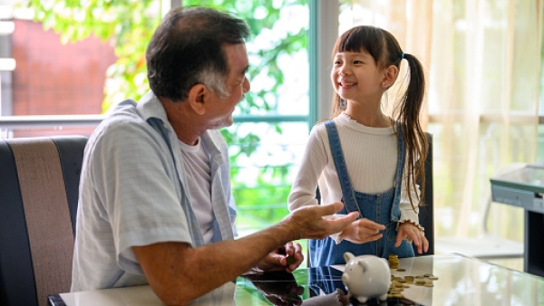 Grandfather and granddaughter counting money with piggy bank.