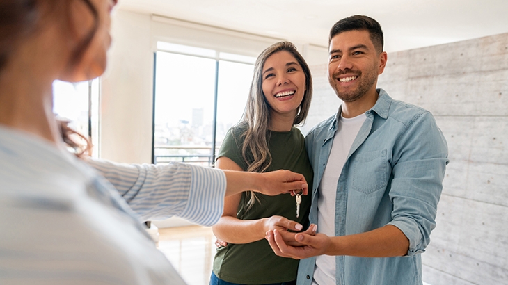 Real estate agent giving the keys of their new house to a happy couple.