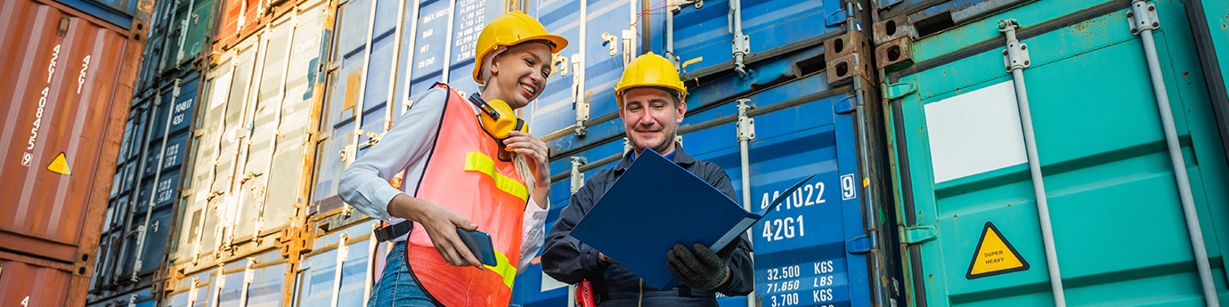 Two people in hardhats talking by shipping containers.