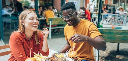 Amigos divirtiéndose comiendo hamburguesas y papas fritas en un restaurante al aire libre.