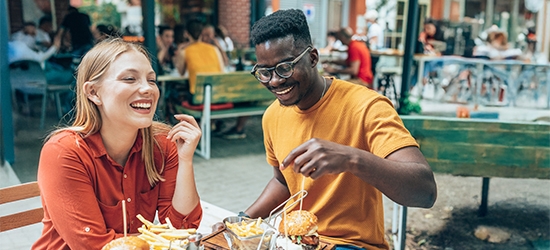 Amigos divirtiéndose comiendo hamburguesas y papas fritas en un restaurante al aire libre.