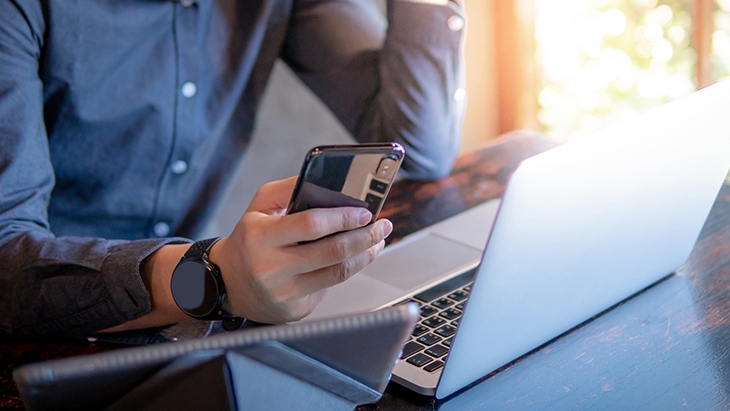 Man looking at phone while using laptop