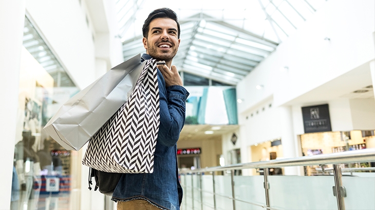 Man walking through a shopping mall with bags.