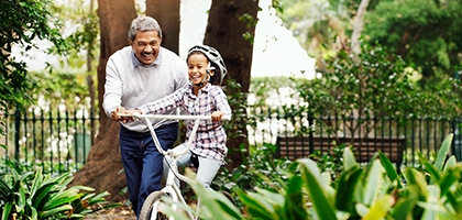 Little girl being taught how to ride a bicycle by her grandfather at the park