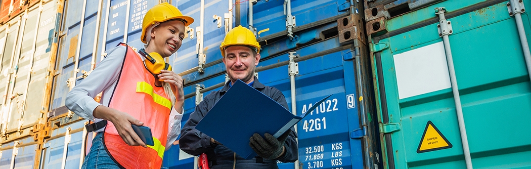 Two people in hardhats talking by shipping containers.