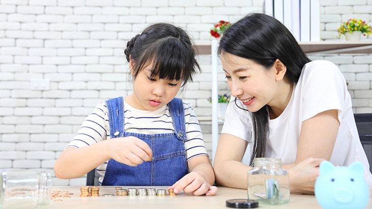 Mother teaching daughter about saving money with coins.