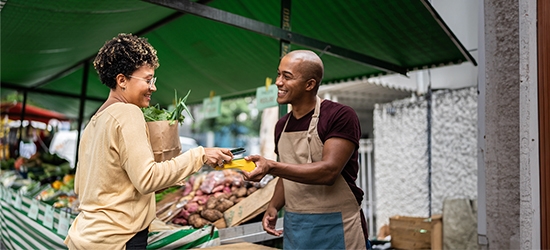 Woman checking out at vegetable stand with a mobile phone.