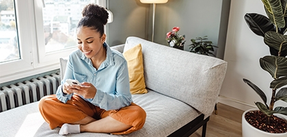 Woman on her mobile phone while sitting cross-legged on a couch.