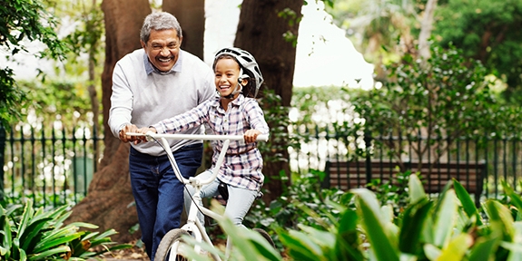 Little girl being taught how to ride a bicycle by her grandfather at the park