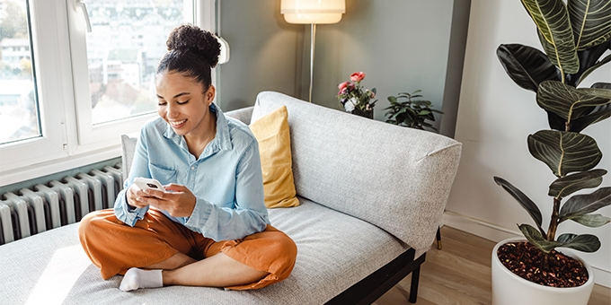 Woman on her mobile phone while sitting cross-legged on a couch.